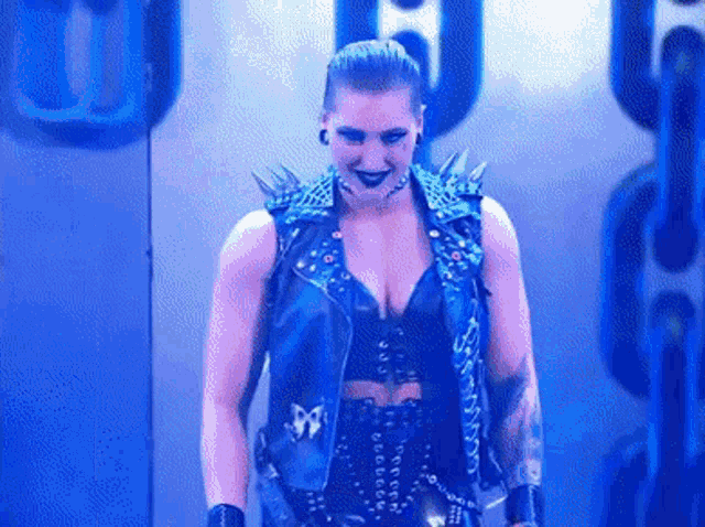 a woman wearing a blue vest with spikes on it is standing in front of a chain .