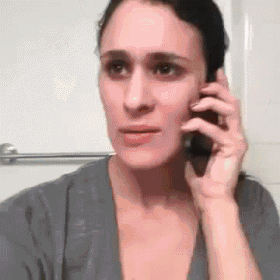 a woman is talking on a cell phone in a bathroom while looking at herself in the mirror .