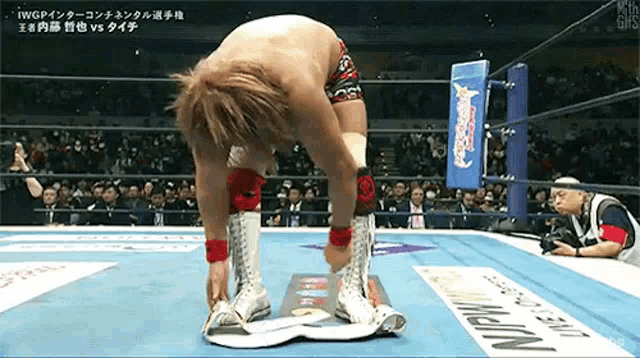 a man is kneeling down in a wrestling ring while a referee looks on .