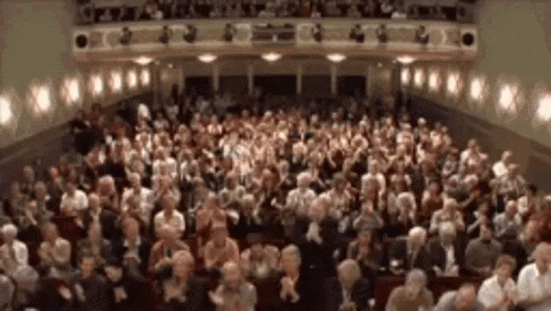 a large group of people are sitting in a theater applauding