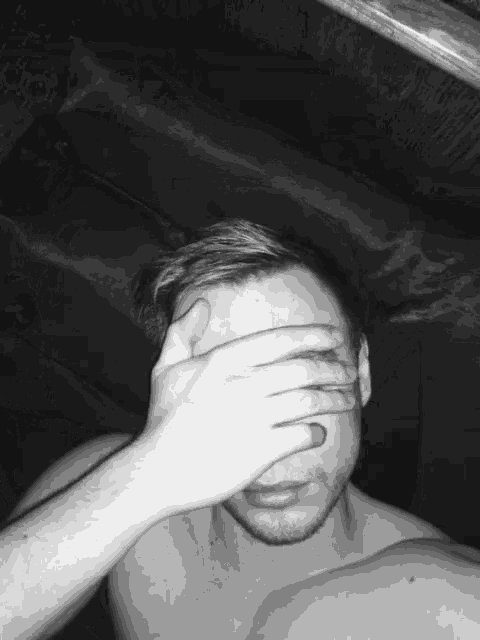 a shirtless man is covering his face with his hand