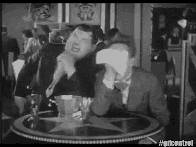 a black and white photo of a man sitting at a table with a cup of coffee and a piece of paper on his face .