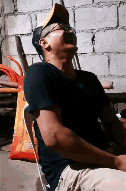 a man wearing a black shirt and a yellow hat is sitting in front of a bag that says ' flavoring '