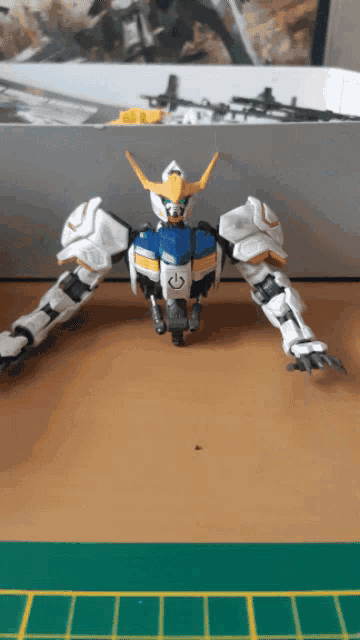 a white blue and yellow robot is sitting on a table with its arms outstretched