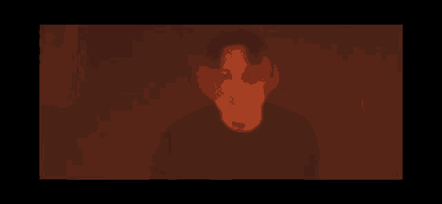 a man in a black shirt is standing in a dark room in a red light .
