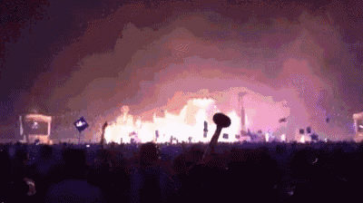 a crowd of people watching a concert with a large fire in the background .
