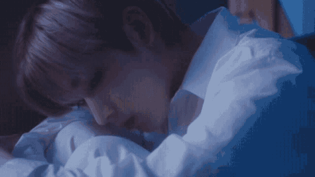 a man in a white shirt is laying on a bed with his head on a pillow .