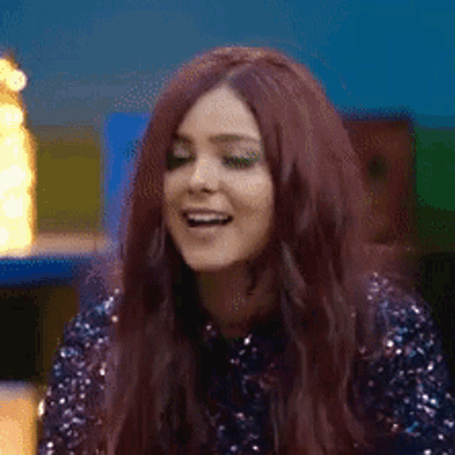 a woman with long red hair is wearing a sequined top and smiling .