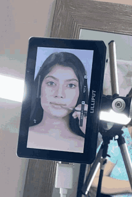 a lilliput screen shows a woman applying makeup to her face