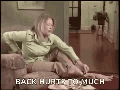 a woman is sitting on a couch with her back in pain and the words `` back hurts to much '' written on the screen .