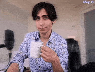 a man in a floral shirt is holding a cup of coffee and the name mary 13 is on the bottom right