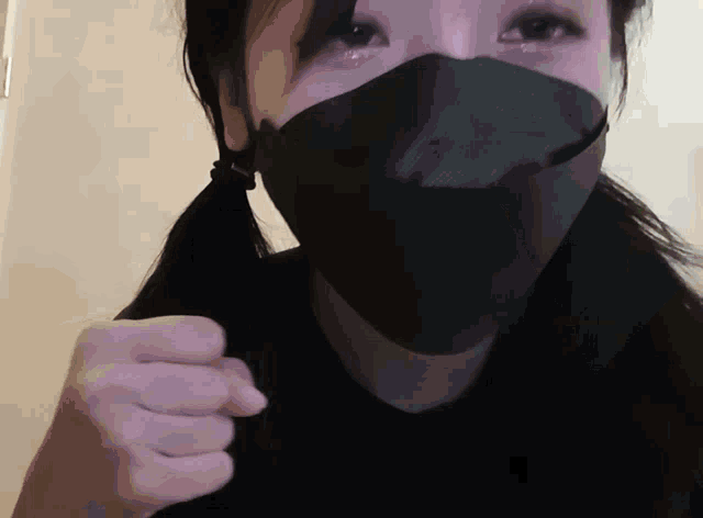 a woman wearing a black face mask holds her fist up in the air