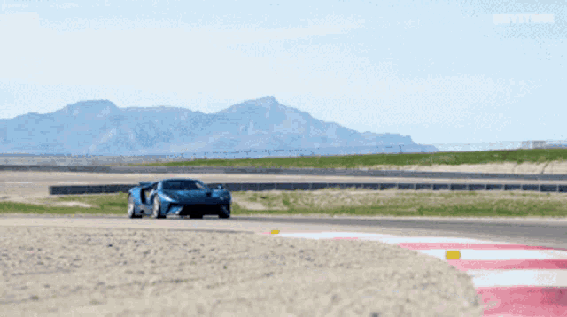 a blue sports car is driving on a track with mountains in the background and the word driftzone on the bottom