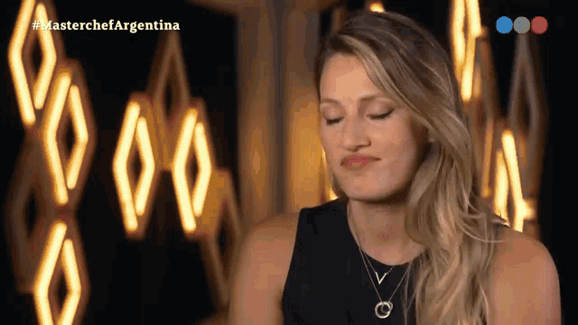 a woman with her eyes closed in front of a sign that says #masterchefargentina