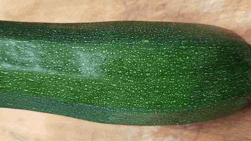 a green zucchini is sitting on a wooden surface