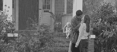 a man and woman are standing in front of a house holding a baby .
