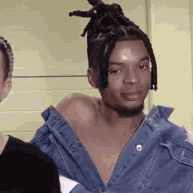 a man with dreadlocks is wearing a denim jacket over his shirt .