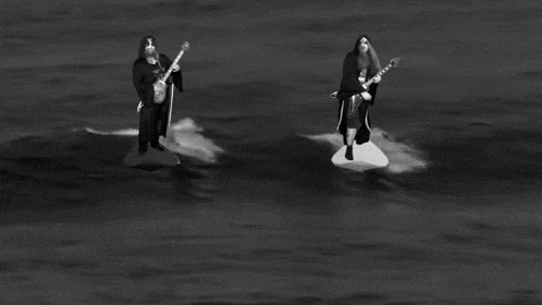 a black and white photo of two men playing guitars in the water