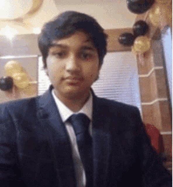 a young man in a suit and tie is standing in front of balloons in a room .