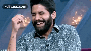 a man with a beard is laughing with his hand in his mouth .