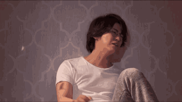 a man wearing glasses and a white shirt is sitting in front of a wall