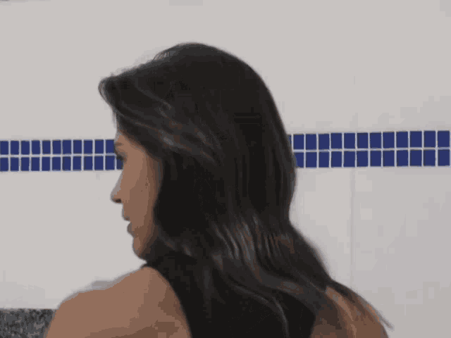 a woman is smiling in front of a white wall with blue squares