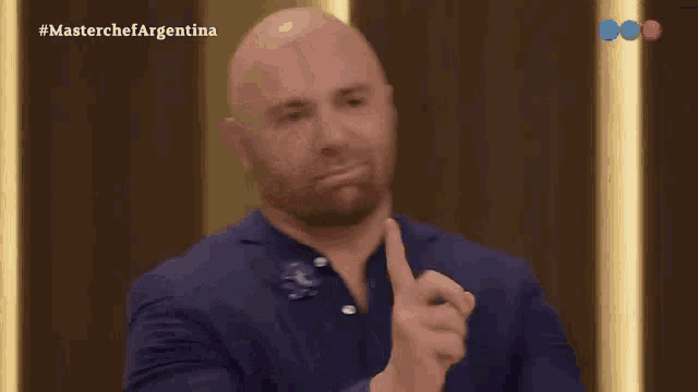 a bald man in a blue suit is giving a thumbs up sign