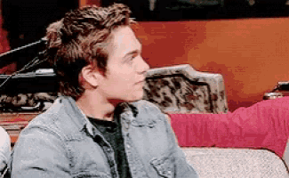 a young man wearing a denim jacket sits on a couch