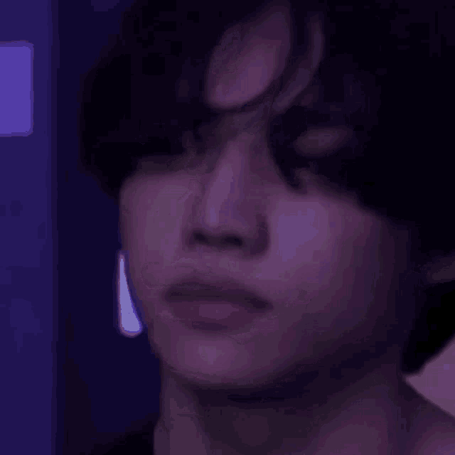 a close up of a person 's face in a dark room with purple lights .