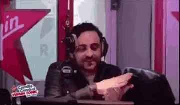 a man wearing headphones is sitting at a desk in front of a microphone in a radio studio .