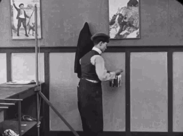 a black and white photo of a man standing in front of a wall with pictures on it
