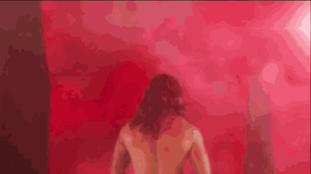 a naked woman is standing in front of a red wall in a room .