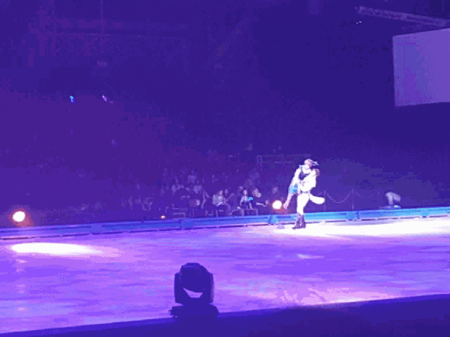 a couple dancing on a ice rink with purple lights