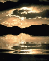 a lake with mountains in the background and the sun shining through the clouds