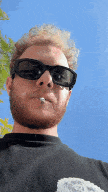 a man with a cigarette in his mouth wears sunglasses