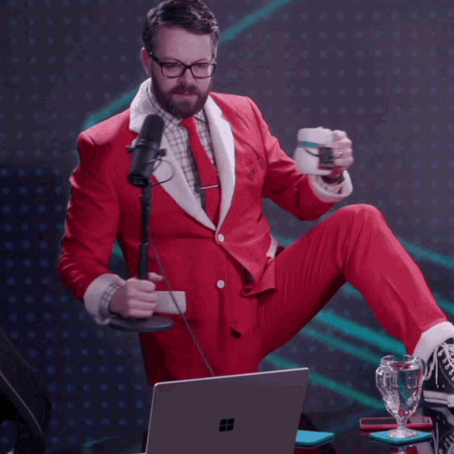 a man in a santa suit is sitting in front of a laptop and holding a cup