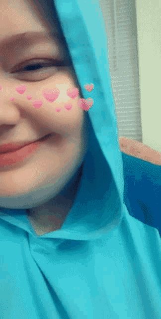 a woman wearing a blue hooded sweatshirt has pink hearts on her face