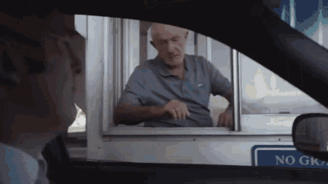 a man in a car talking to another man behind a window with a sign that says no gk