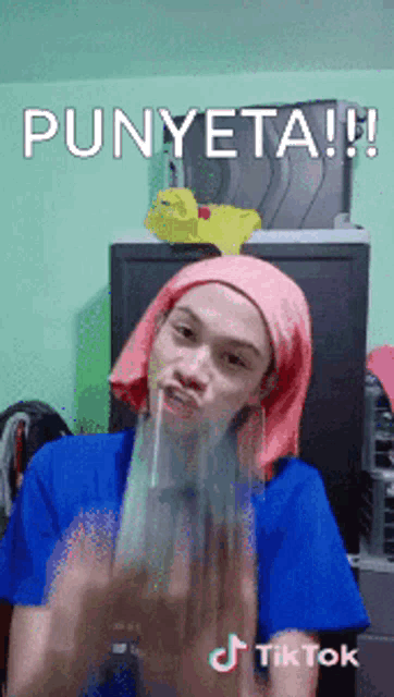 a woman wearing a pink head scarf and a blue shirt is making a funny face and says punyeta !!!