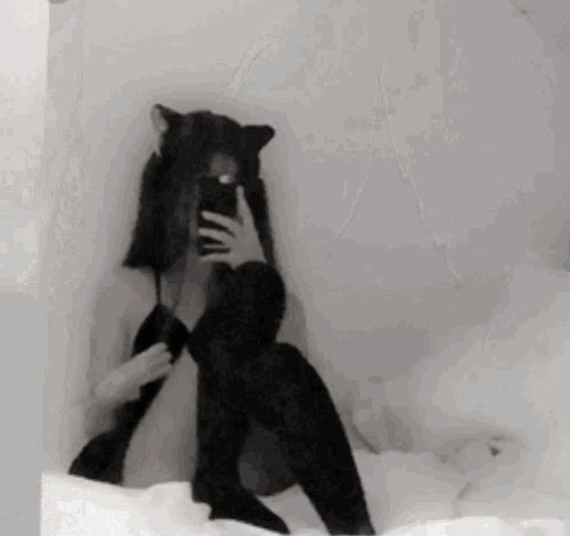 a woman is sitting on a bed taking a picture of herself in the mirror .