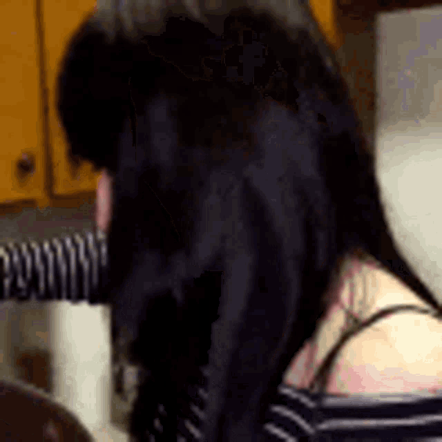 a woman with long black hair is sitting in a kitchen with a striped shirt on .