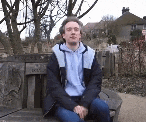 a man sits on a bench with a sign that says the queens round