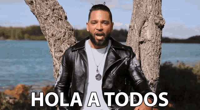 a man in a black leather jacket is standing next to a tree and says hola a todos