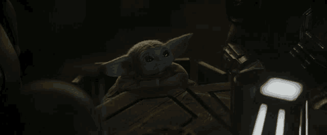 a baby yoda sits in a dark room