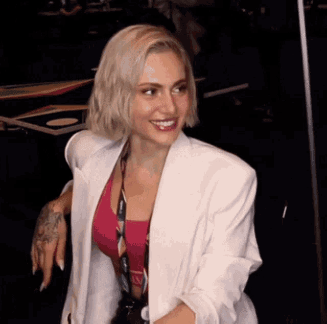 a woman in a white jacket and pink top is smiling