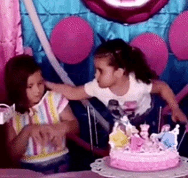 two little girls are playing with a pink birthday cake