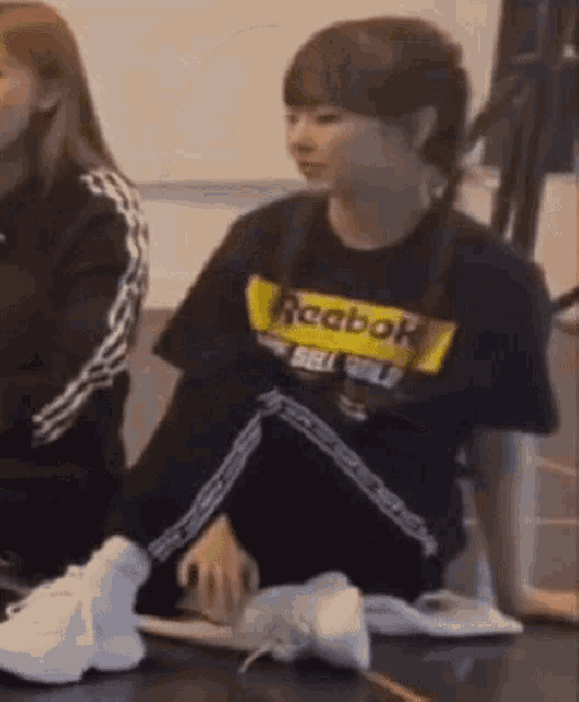 a girl wearing a black reebok shirt is sitting on the floor .