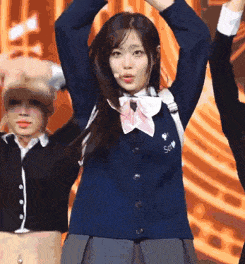 a girl in a school uniform is dancing on a stage with her arms in the air