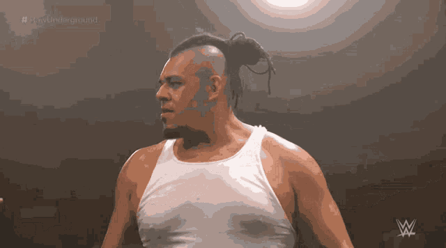 a man in a white tank top stands in front of a sign that says ' wwe underground '