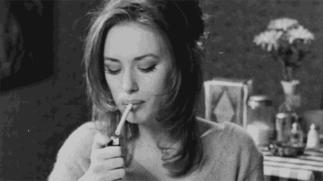 a black and white photo of a woman lighting a cigarette .